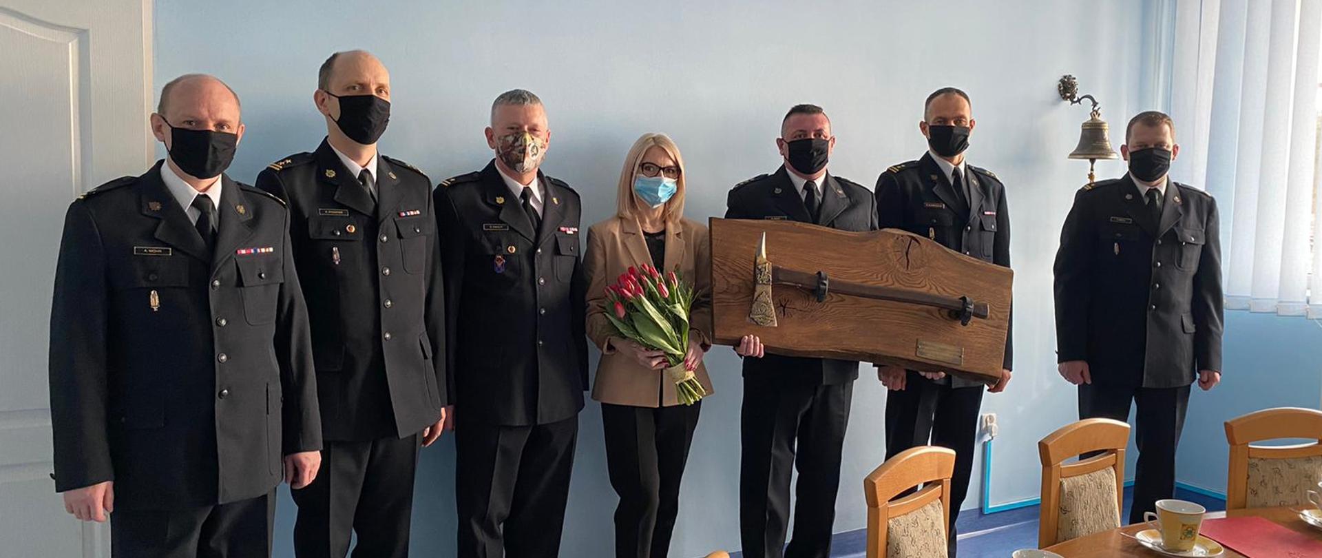 Zdjęcie przedstawia funkcjonariuszy ubranych w mundury wyjściowe podczas uroczystego zdjęcie w związku z przejściem jednego funkcjonariusza na zaopatrzenie emerytalne