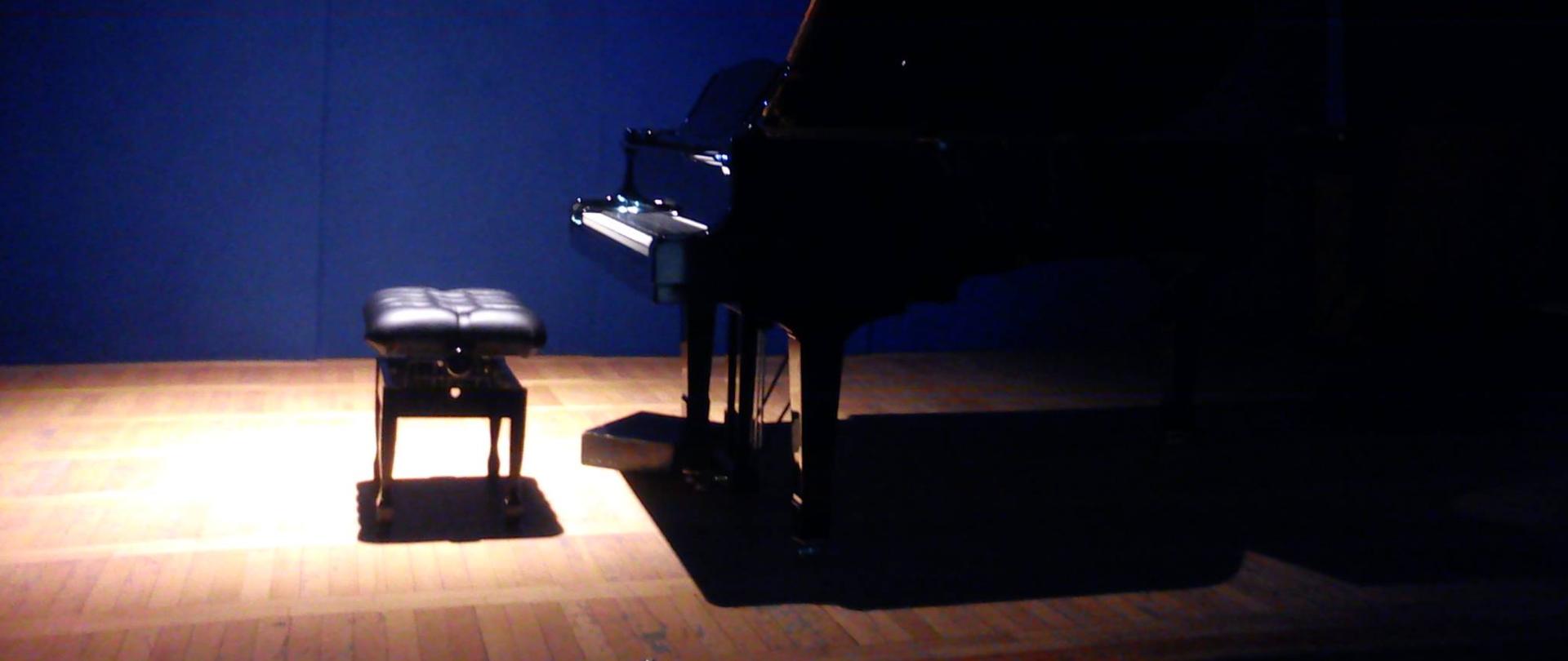 zdjęcie fortepianu na scenie w zaciemnionym otoczeniu