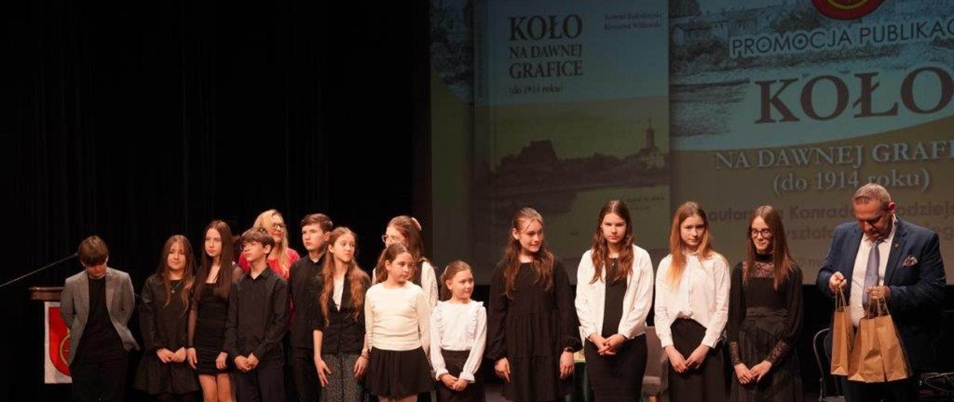 na scenie uczniowie biorący udział w koncercie wraz z nauczycielką i burmistrzem miasta