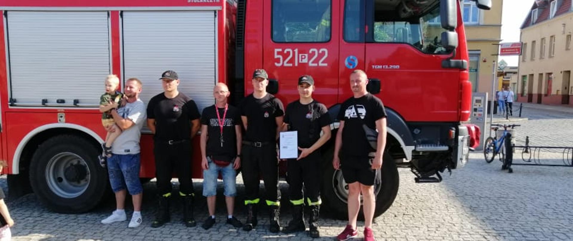 Zdjęcie przedstawia funkcjonariuszy PSP wraz z przedstawicielami Klubów pojazdów zabytkowych na tle samochodu strażackiego.