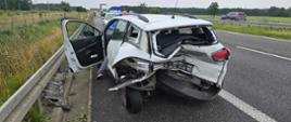 Na pasie awaryjnym stoi białe auto z mocno uszkodzonym tyłem