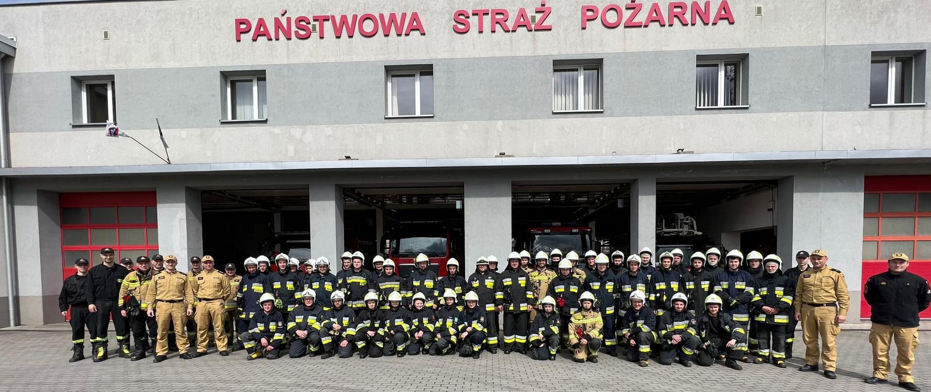 Zdjęcie grupowe funkcjonariuszy Komendy Powiatowej Państwowej Straży Pożarnej w Lęborku oraz uczestników egzaminu końcowego szkolenia podstawowego strażaków ratowników Ochotniczych Straży Pożarnych przed budynkiem komendy.