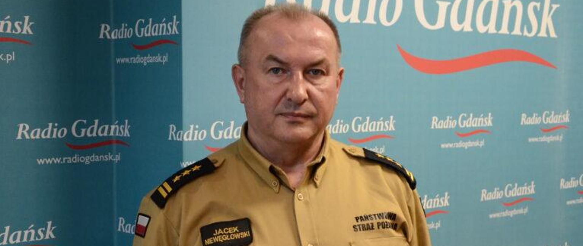 Mężczyzna w mundurze musztardowym stoi na tle napisu Radio Gdańsk.