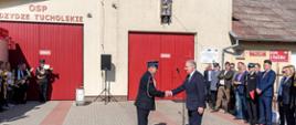 Strażak Ochotniczej Straży Pożarnej we Wdzydzach Tucholskich wita się z wojewodą pomorskim w obecności zaproszonych gości.