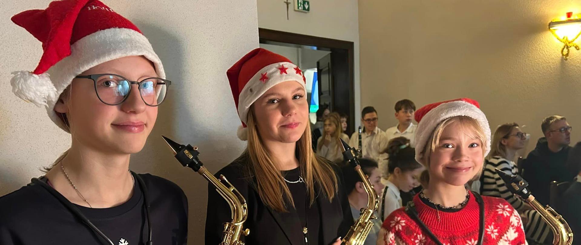 trzy uczennice grające na saksofonach w mikołajowych czapeczkach