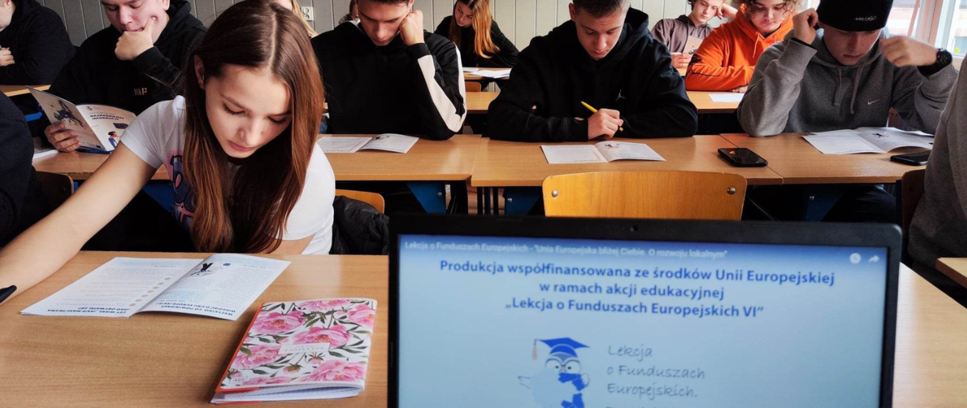 Młodzież w ławkach szkolnych czyta publikację