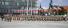 Na zdjęciu znajdują się żołnierze Wojska Polskiego. W tle znajduje się kilkanaście biało-czerwonych flag oraz fragment okolicznego biurowca.