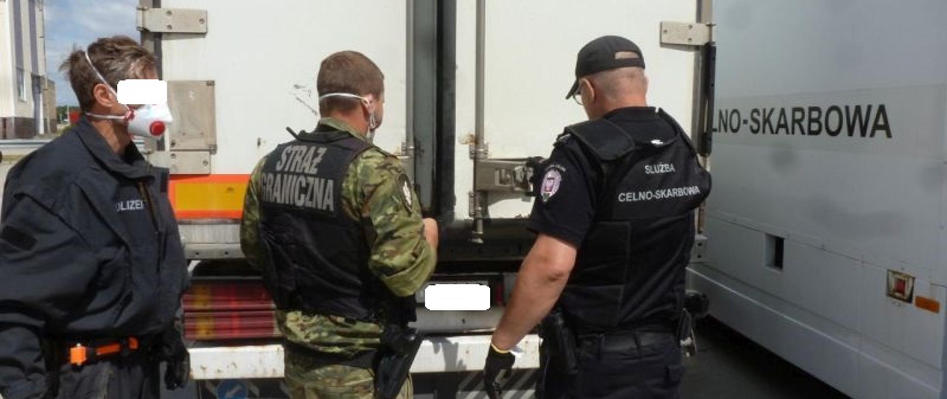 Funkcjonariusze Policji, Straży Granicznej i Służby Celno-Skarbowej z tyłu naczepy samochodu ciężarowego.