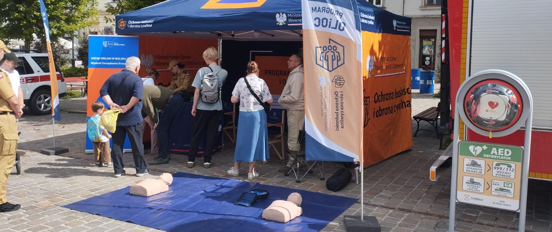 Plenerowe stoisko obrony cywilnej i MSWiA na rynku. Na macie fantomy do pierwszej pomocy, obok AED.