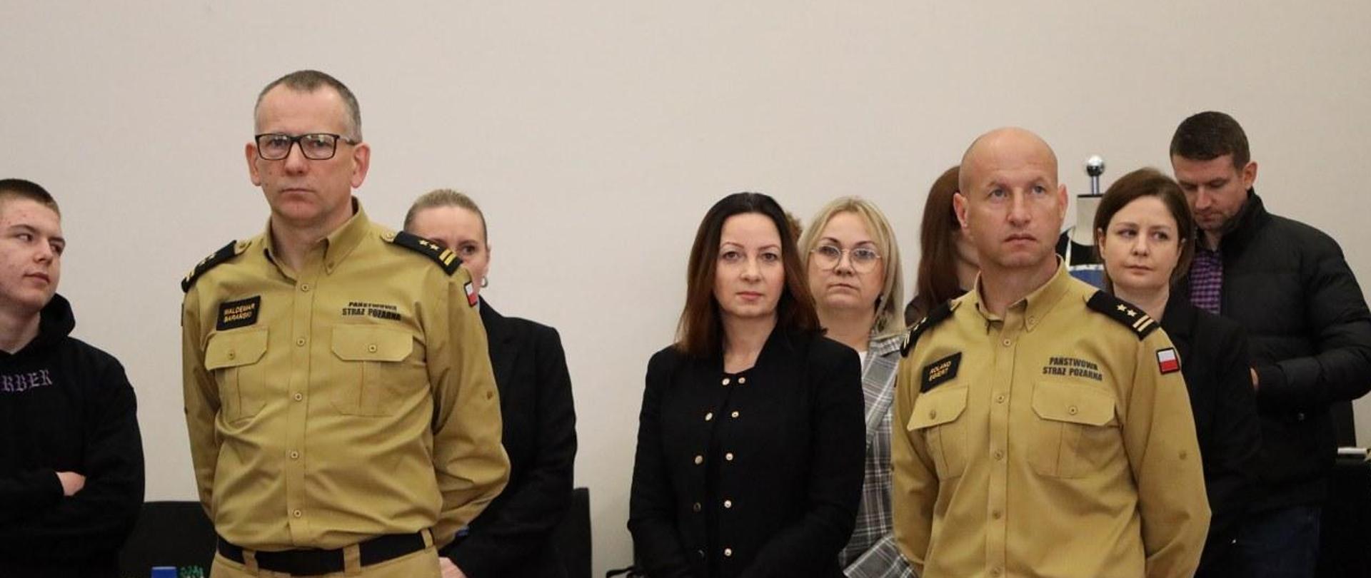 Dwóch strażaków wraz z innymi ludźmi podczas wydarzenia.