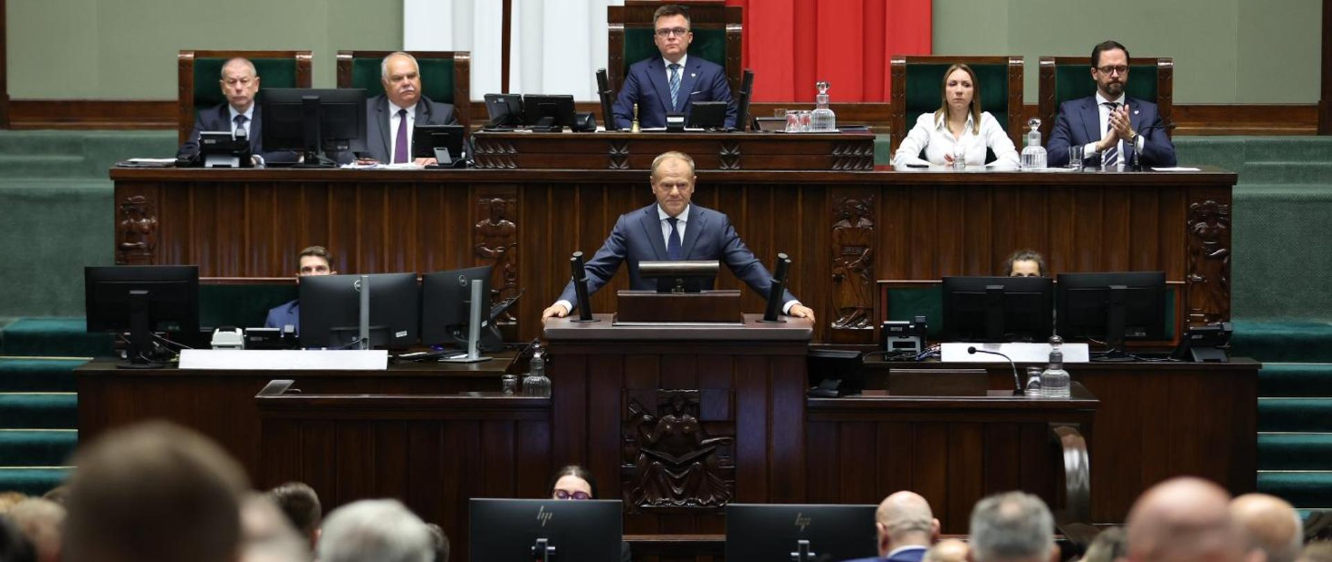 Premier Donald Tusk podczas wystąpienia w Sejmie w związku z naruszeniem polskiej przestrzeni powietrznej, 10.09.2025 r. W tle Marszałek Sejmu Szymon Hołownia. (fot. https://www.gov.pl/web/premier/naruszenie-polskiej-przestrzeni-powietrznej-jest-wniosek-o-uruchomienie-art-4-traktatu-polnocnoatlantyckiego)