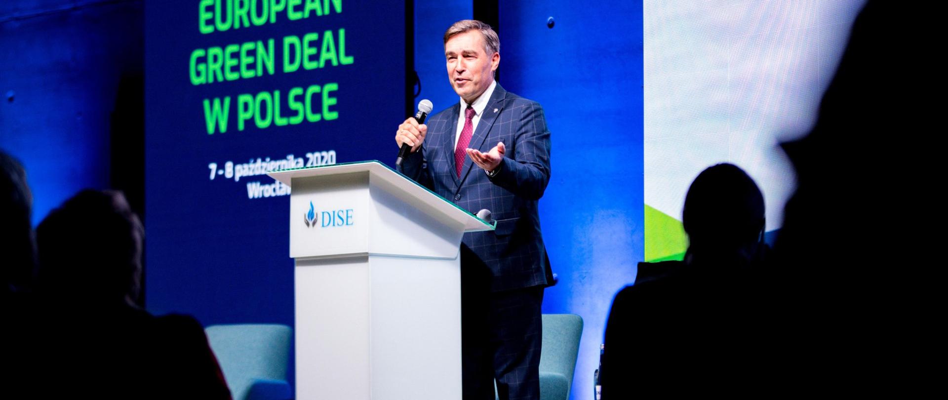 Wiceminister Zbigniew Gryglas przemawia z mównicy na tle ekranu z nazwą konferencji.