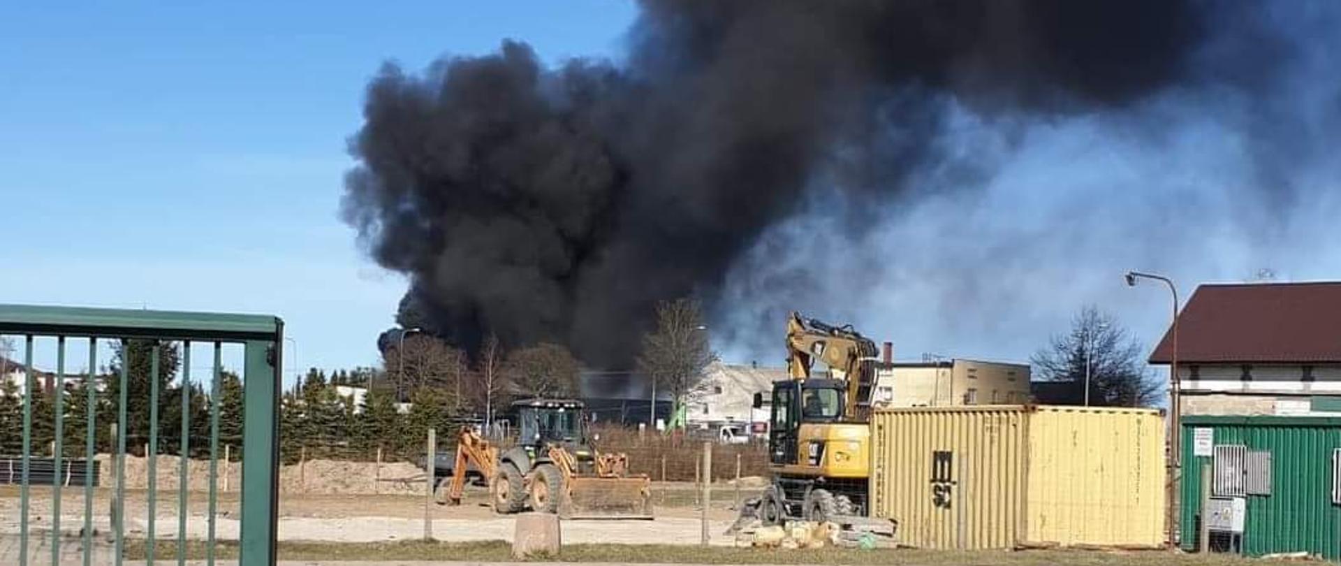 Czarny, gęsty dym unoszący się nad terenem zakładu produkcyjnego.