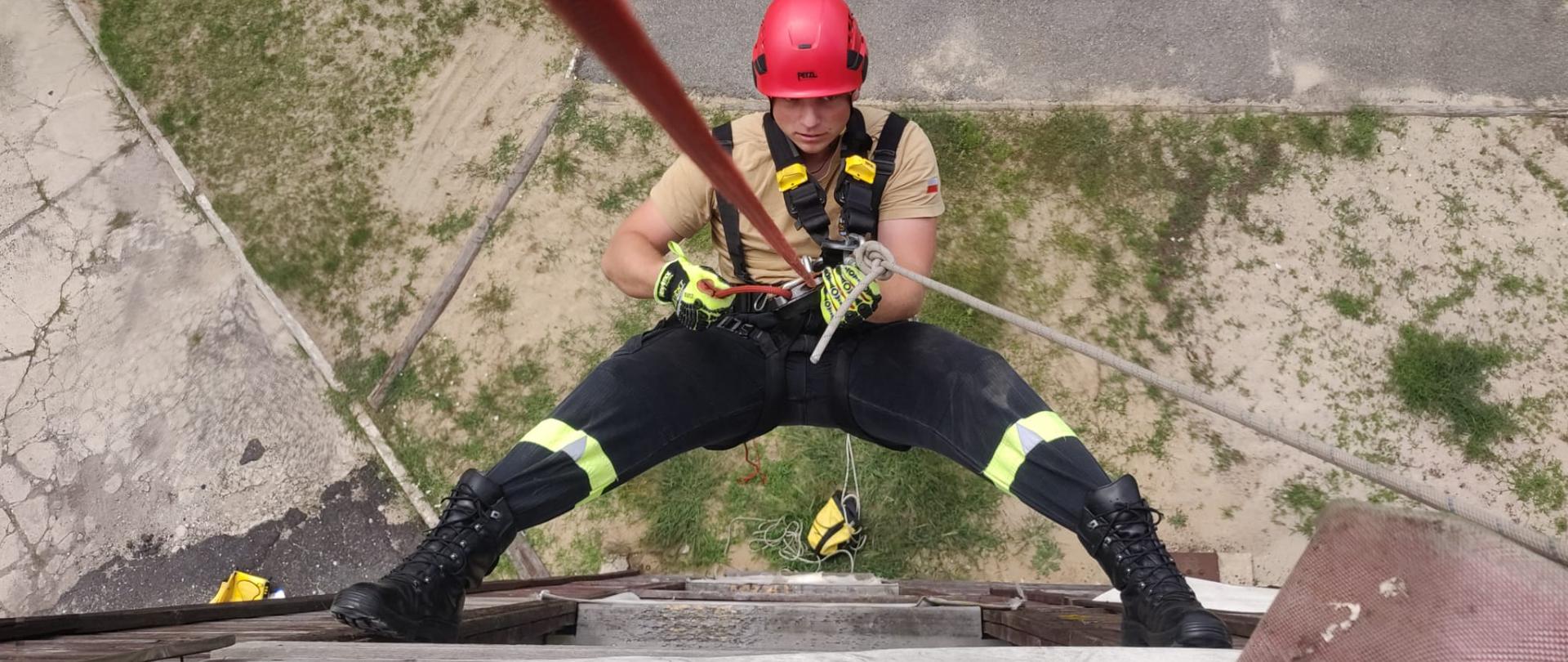 Na zdjęciu znajduje się strażak puszczający się na linie ze wspinalni