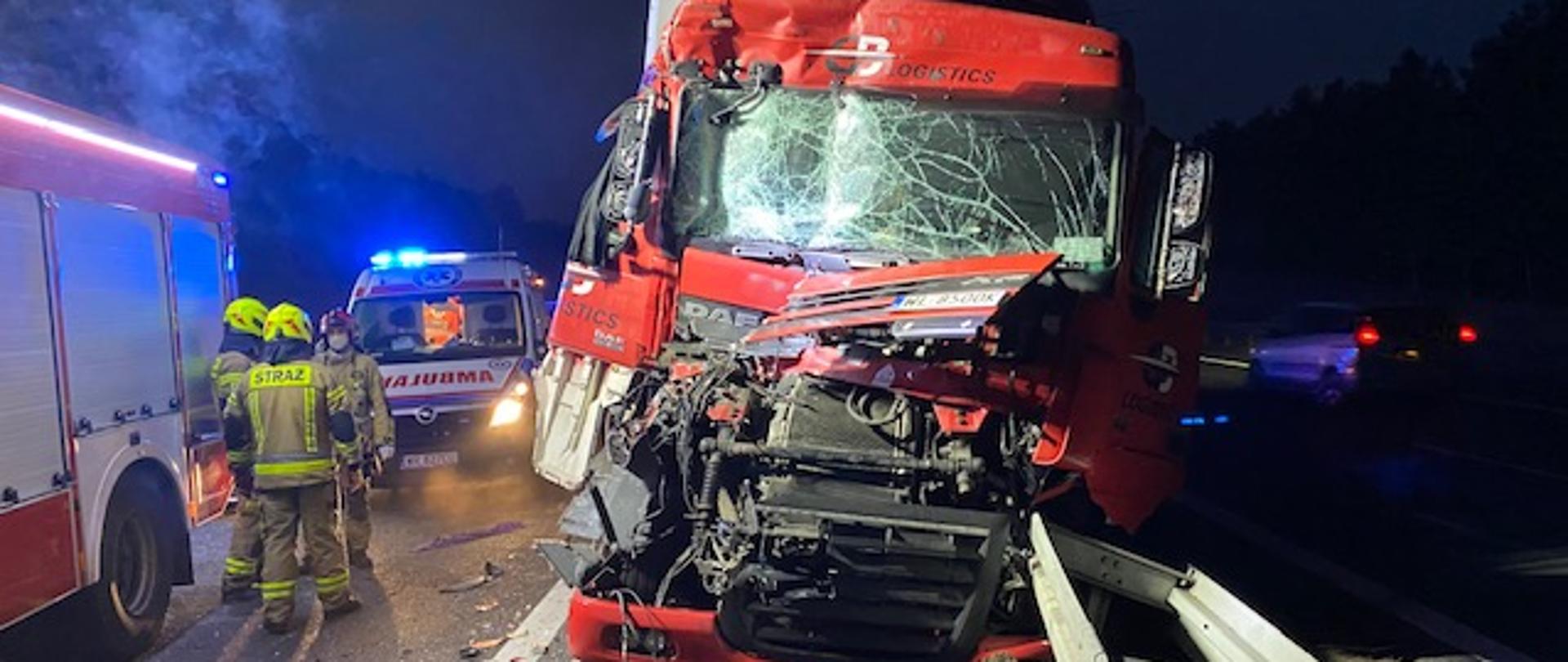 Zdjęcie przedstawia rozbity pojazd ciężarowy marki DAF oparty o zniszczone barierki oddzielające pasy ruchu na 109 km trasy S3 w kierunku Gorzowa. Obok stoi 3 strażaków. Za nimi
Karetka pogotowia.