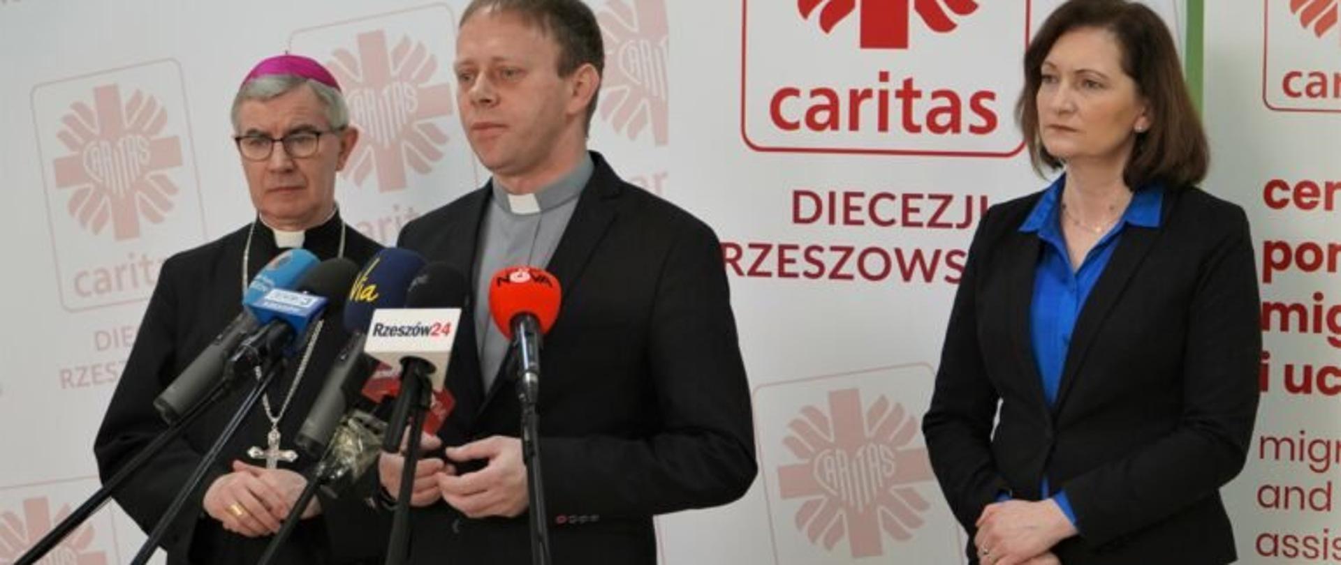 Dyrektor Caritas Diecezji Rzeszowskiej Piotr Potyrała zabiera głos podczas konferencji prasowej podsumowującej rok pomocy dla Uchodźców. W tle biskup rzeszowski Jan Wątroba i wojewoda podkarpacki Ewa Leniart