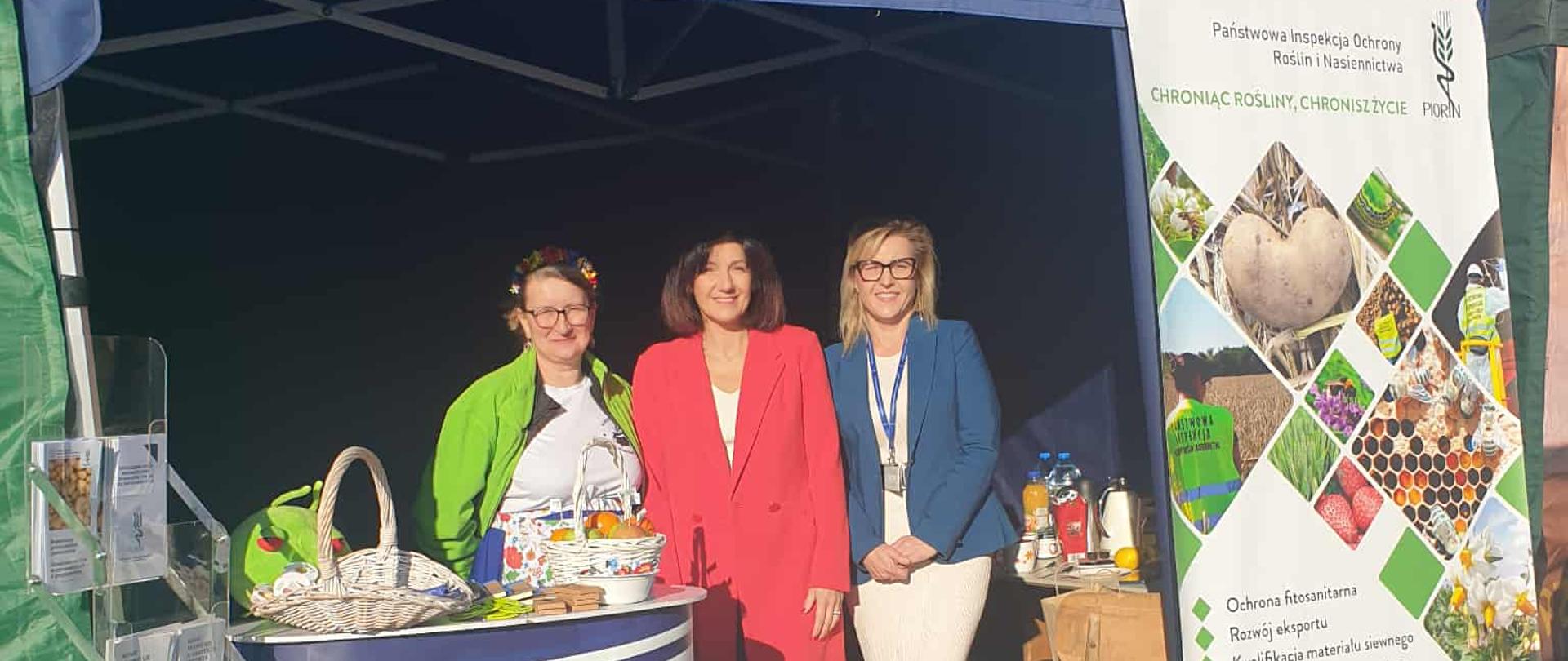 Trzy uśmiechnięte kobiety stoją w namiocie handlowym inspekcji