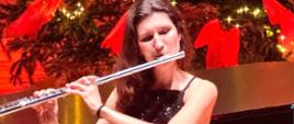 Kobieta gra na flecie. W tle widać udekorowana choinkę.
