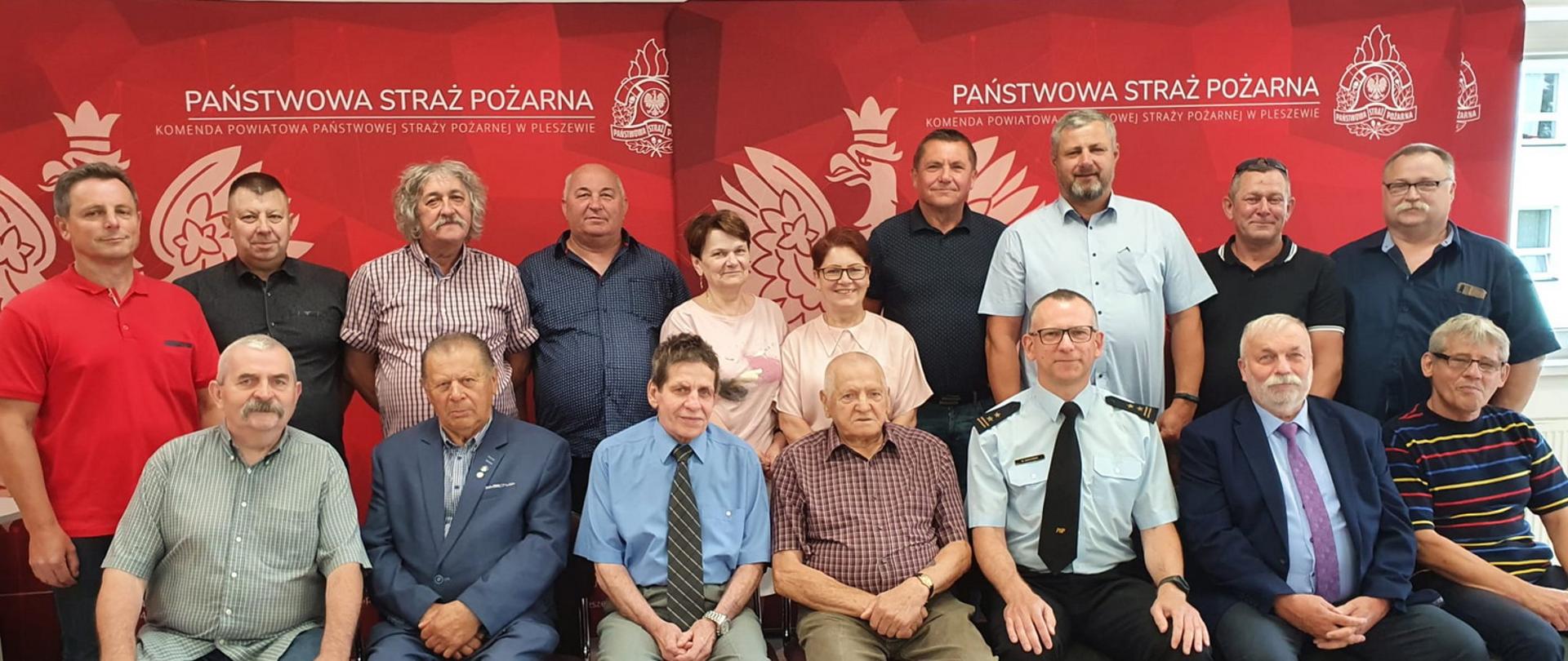 Zdjęcie grupowe osób ustowiomych w dwóch rzędach, pierwszy rząd siedzi na krzesłach, w tle czerwone ścianki reklamowe z napisem Państwowe Straż Pożarna