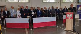 Na trybunie honorowej zaproszeni na Uroczystość goście /Po prawej stronie na mównicą przemawiający Komendant Powiatowy PPS w Krapkowicach w mundurze galowym, bez czapki. uroczystość odbywa się na garażu JRG. 