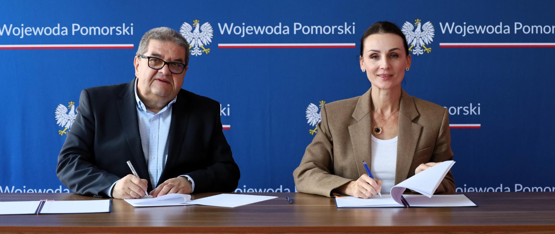 dwie osoby - kobieta i mężczyzna siedzą przy biurku i podpisują dokumenty