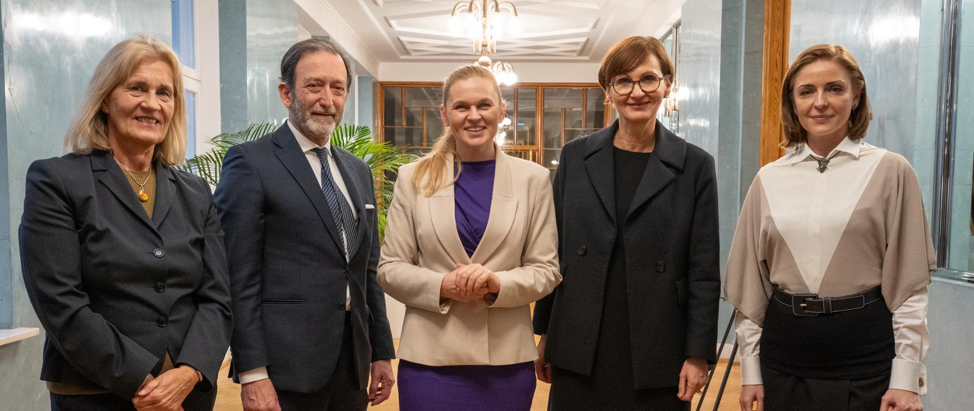 Na zdjęciu widoczne jest pięć stojących osób - Minister Edukacji Narodowej Barbara Nowacka, wiceminister Joanna Mucha oraz minister edukacji i badań naukowych Niemiec Bettina Stark-Watzinger wraz z delegacją.