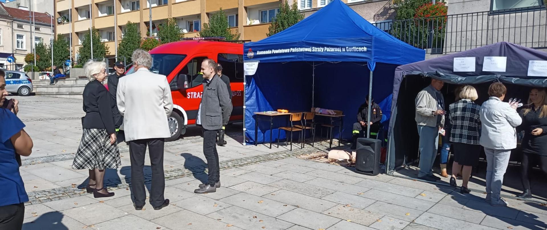 Na zdjęciu widoczna grupa osób dorosłych uczestniczących w I gorlickich dniach seniora przed namiotem koloru niebieskiego z napisem Komenda Powiatowa PSP w Gorlicach pod którym strażacy prowadzili prelekcje z zakresu bezpieczeństwa przeciwpożarowego i pierwszej pomocy.
