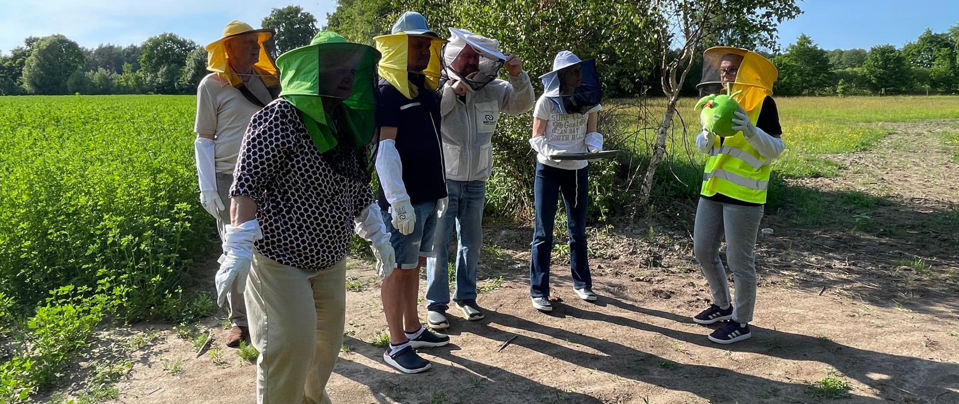 Ubrana w zieloną kamizelkę kobieta opowiada o znaczeniu PESTY maskotki kampanii PH4L obecnym na spotkaniu osobom