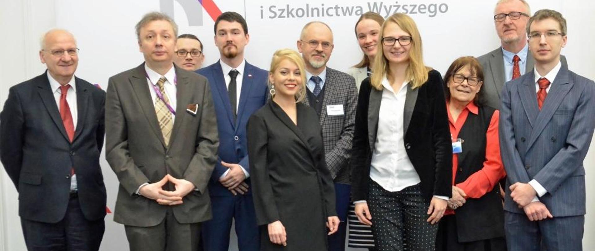 Minister Skuza w otoczeniu laureatów stoi na tle ściany z logiem MNiSW