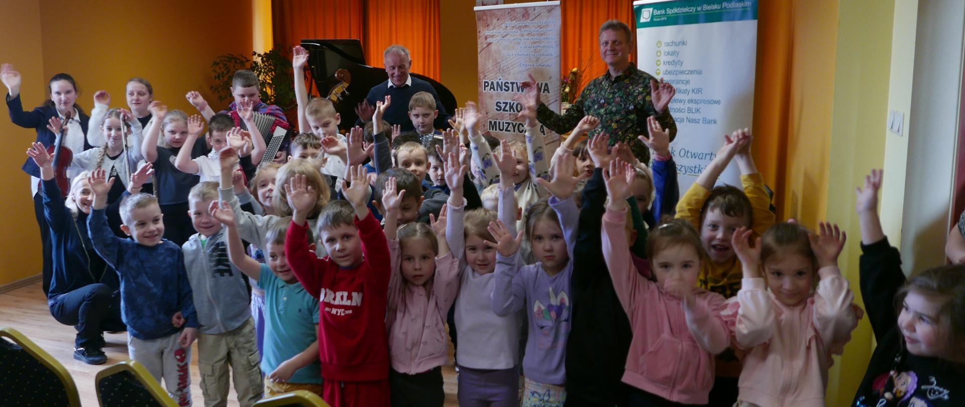 Grupa zadowolonych przedszkolaków na wspólnym zdjeciu z uczniami i nauczycielami szkoły muzycznej.