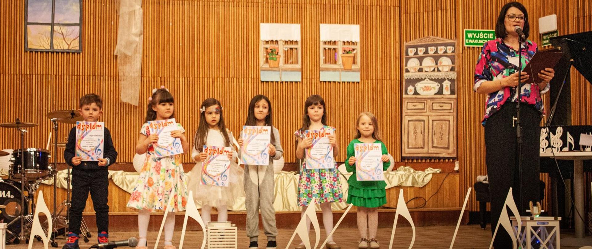 Szóstka dzieci na scenie ZSM w Krośnie, trzymających dyplomy, po prawej stronie prowadząca Kinga Przystasz