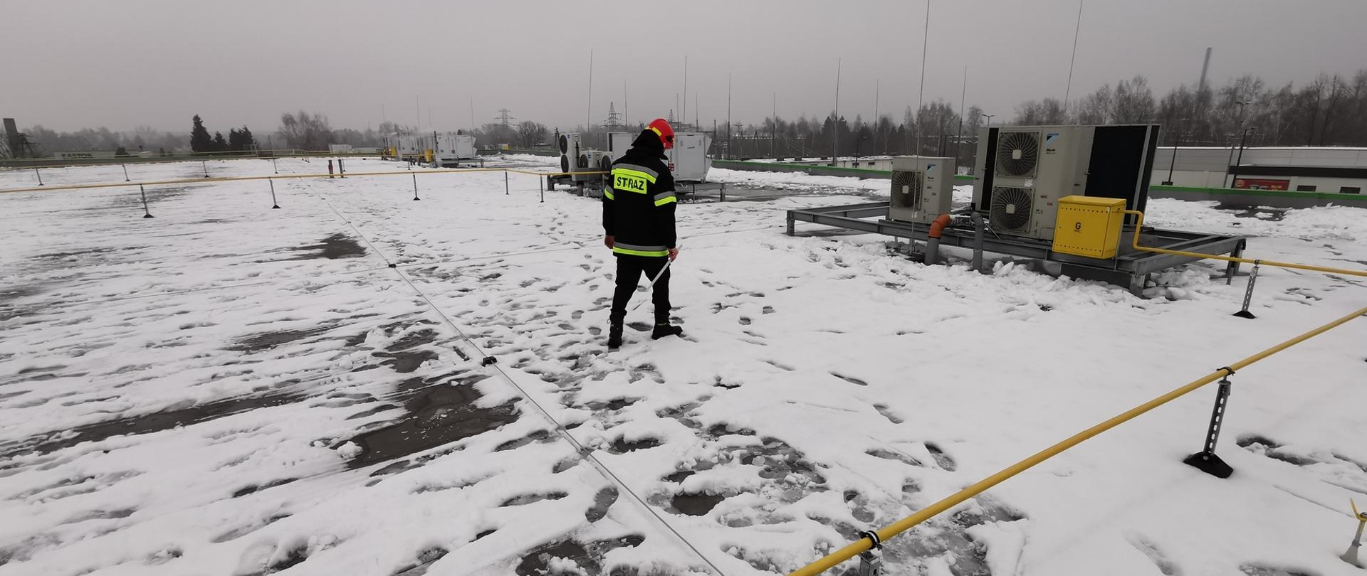 Zdjęcie przedstawia strażaka kontrolującego dach sklepu wielkopowierzchniowego pod kątem ilości 