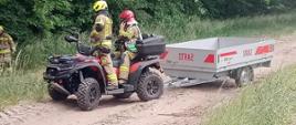 Ćwiczenia WOO. Teren Leśnictwa Górzno. Na drodze gruntowej znajdującej się przy lesie stoi pojazd quad z przyczepką. Na pojeździe jest dwóch strażaków, jeden w żółtym, a drugi w czerwonym hełmie. W tle las.