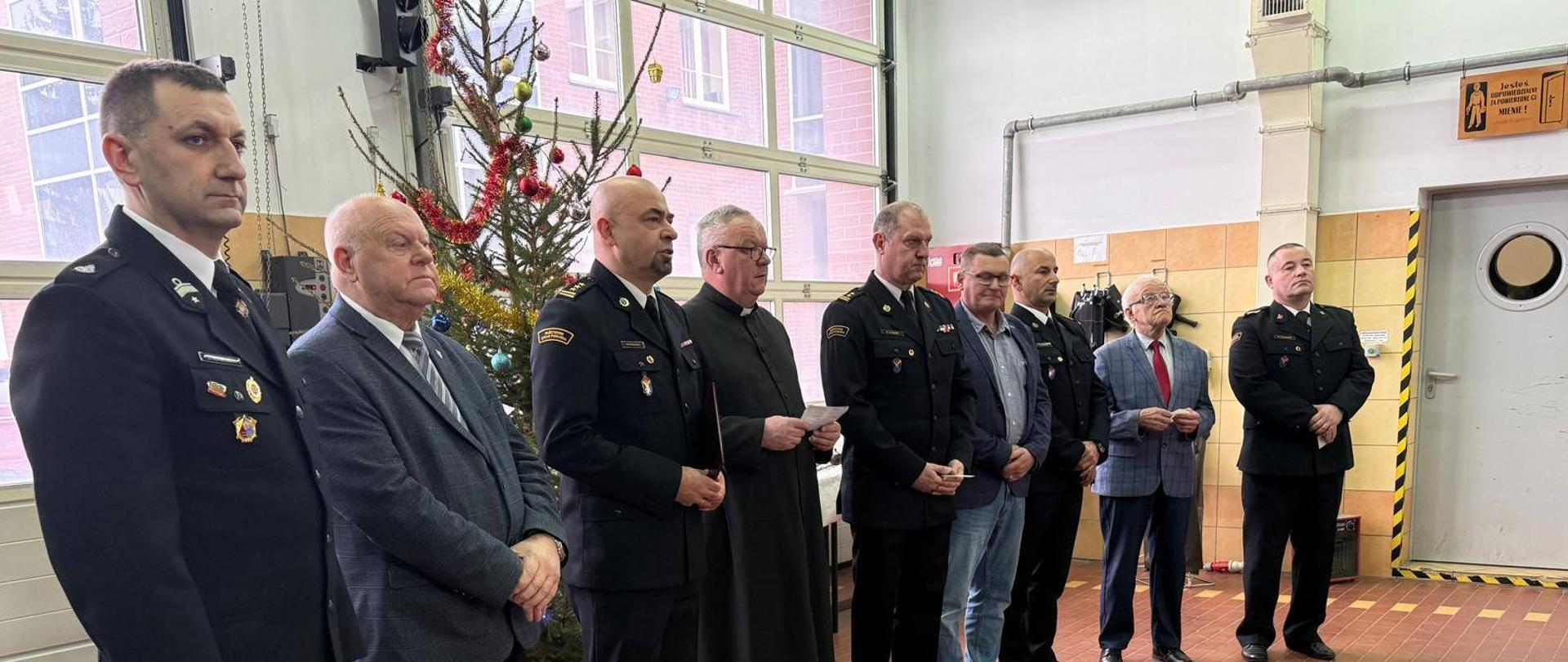 Zdjęcie przedstawia funkcjonariuszy straży, gminy i kościoła zebranych na garażu JRG w Kamieńiu Pomorskim