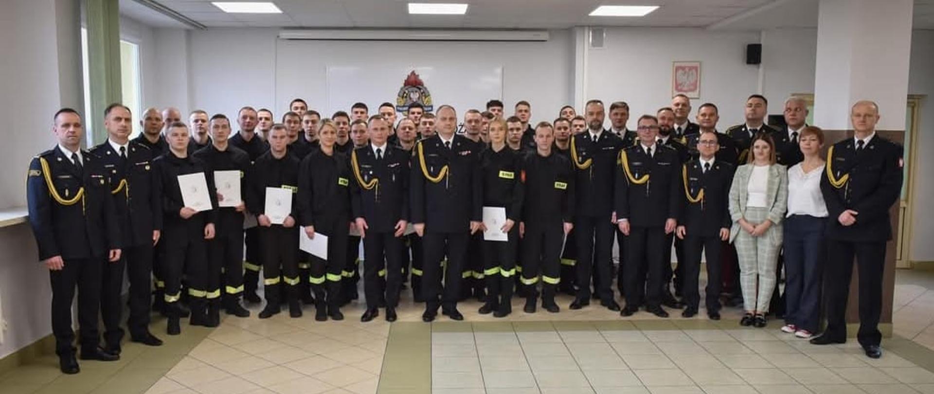 Pamiątkowe zdjęcie grupowe uczestników szkolenia podstawowego w zawodzie strażak z oficerami PSP oraz cywilnymi pracownikami ośrodka szkolenia uczestniczącymi w uroczystości zakończenia szkolenia