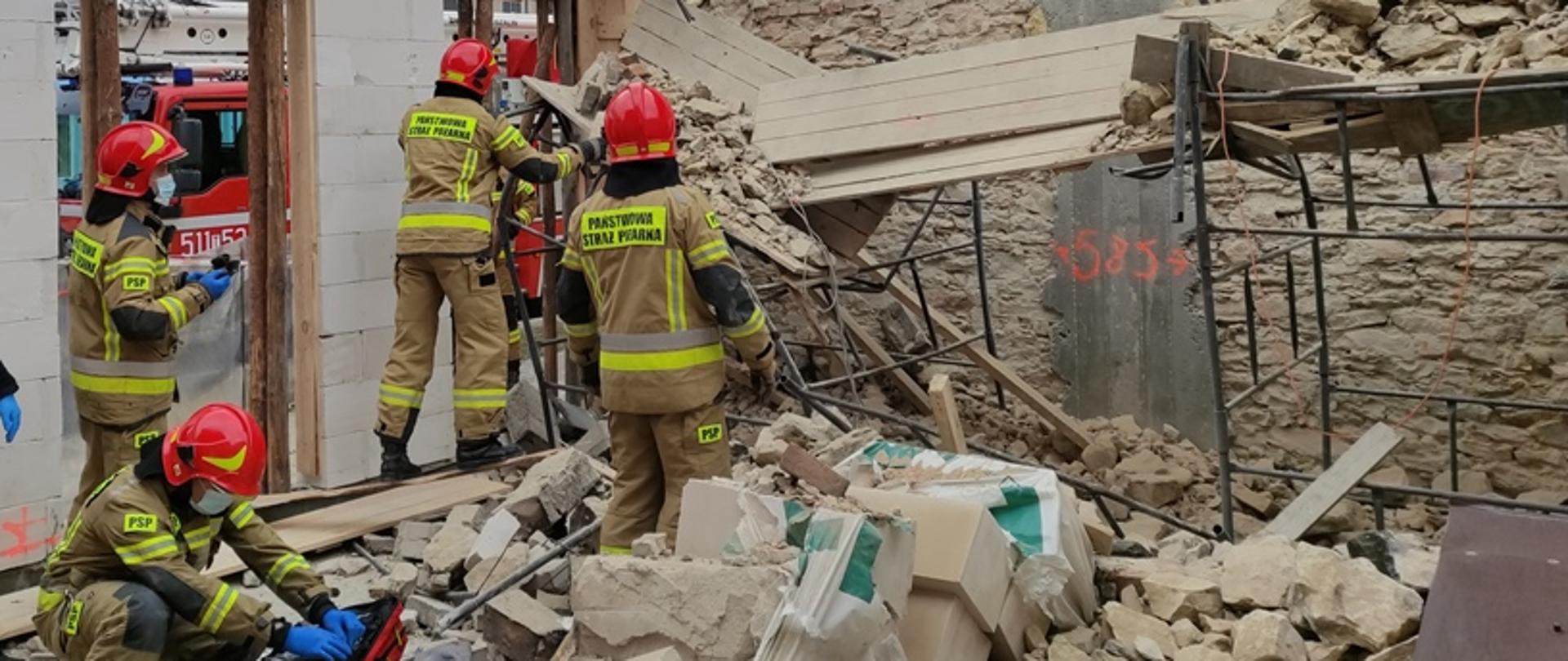 Na zdjęciu strażacy, wewnątrz obiektu będącego w trakcie budowy, prowadzą prace polegające na przeszukaniu gruzowiska.
