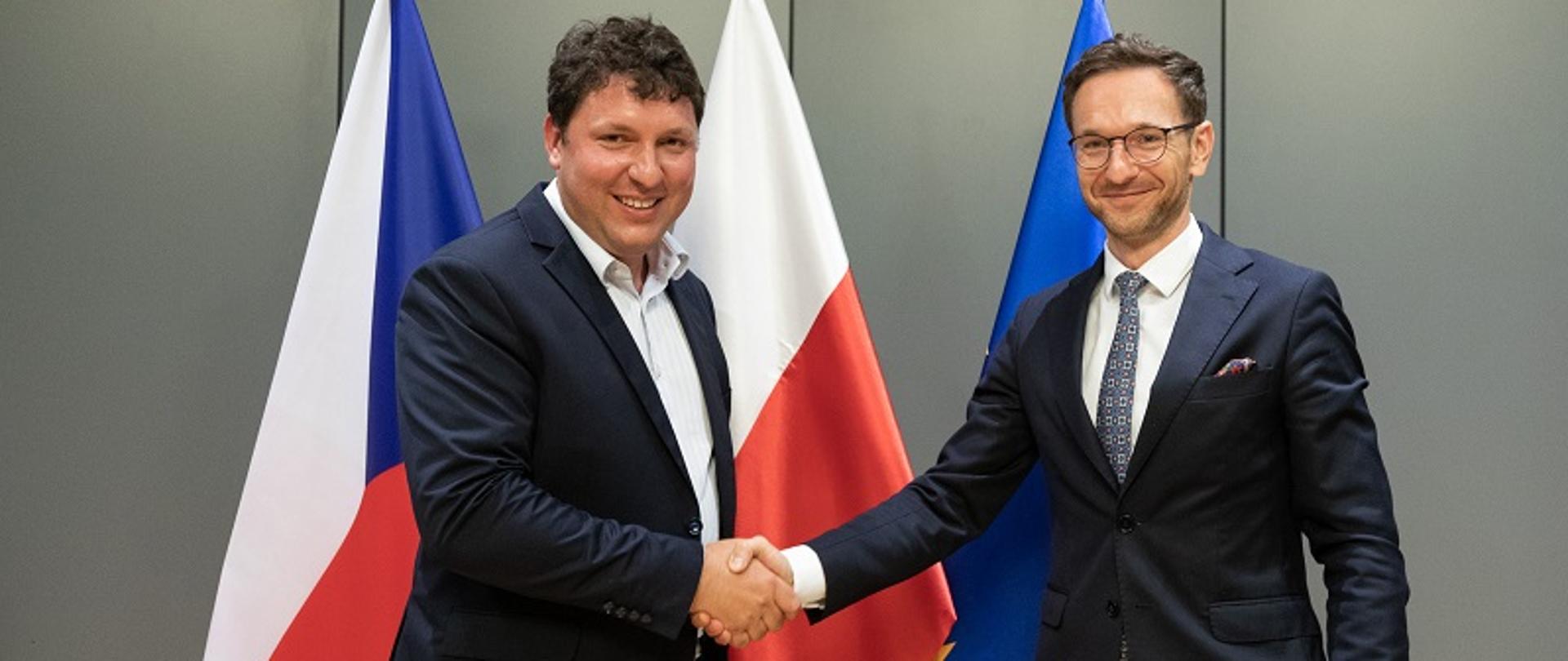 Ministrowie Marian Piecha oraz Waldemar Buda podają sobie dłonie na tle flag Czech i Polski