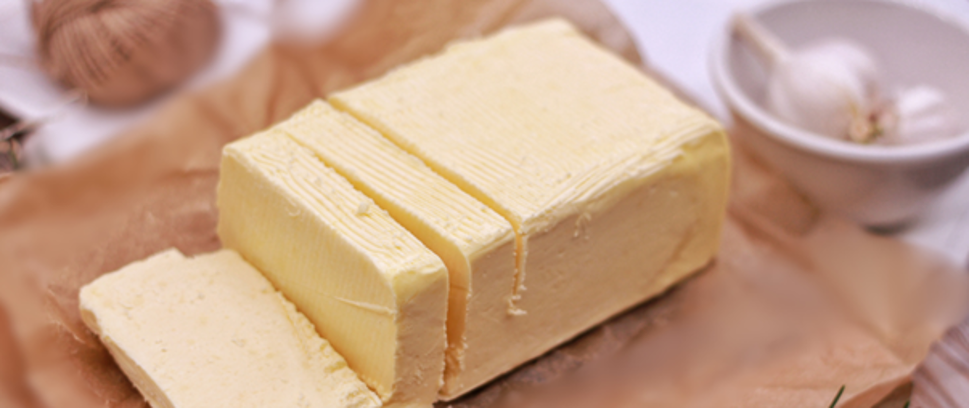 Na pierwszym planie kostka masła, która leży na papierze śniadaniowym, a obok w miseczce widoczny jest ząbek czosnku.