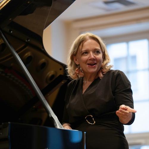 zdjęcie przedstawia prowadzącą warsztaty przemawiającą do publiczności przy podniesionym skrzydle fortepianu na scenie sali koncertowej, inne ujęcie z bliska