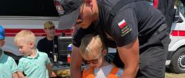 Dzieci oglądają sprzęt używane przez grupę nurkową, jednemu z nich strażak zakłada kamizelkę ratunkową