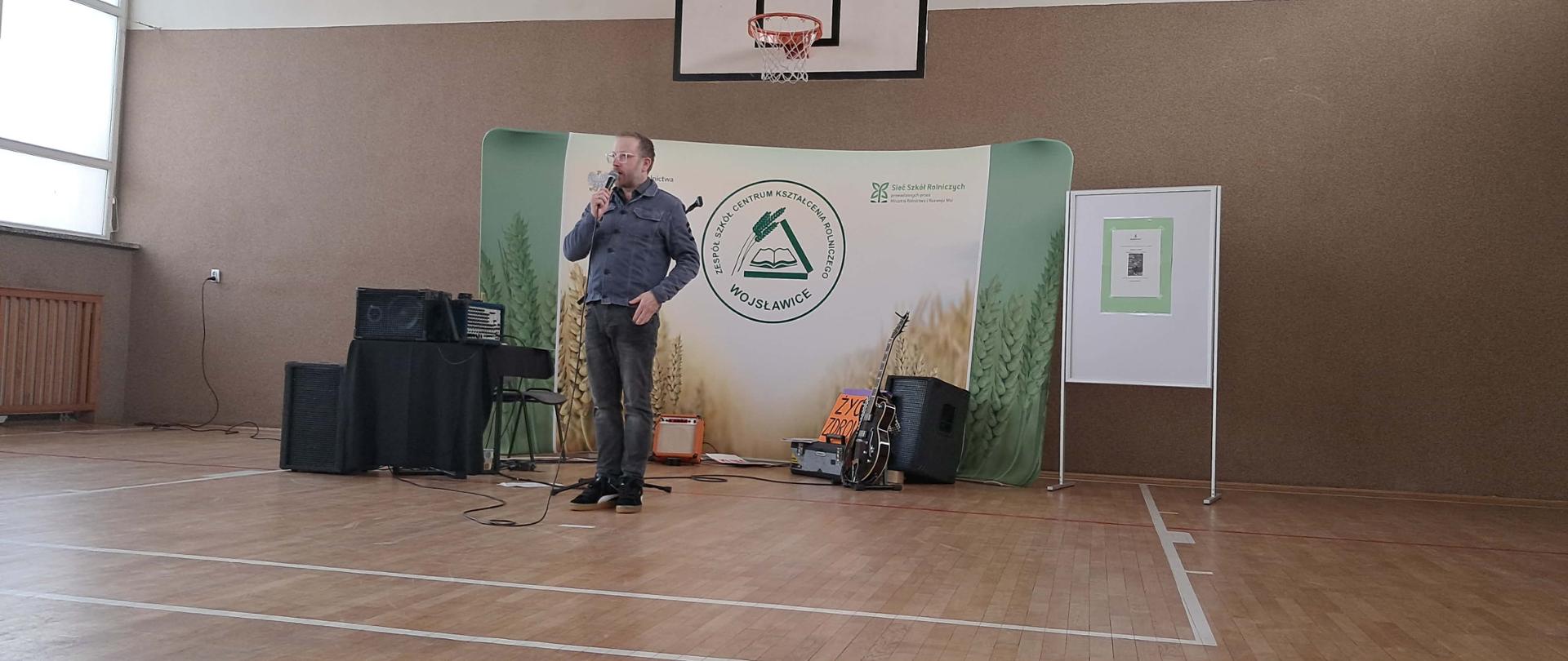 Pan Krzysztof Niedźwiecki przemawia do zgromadzonych uczniów, a sala wypełniona jest spokojną i skupioną atmosferą.