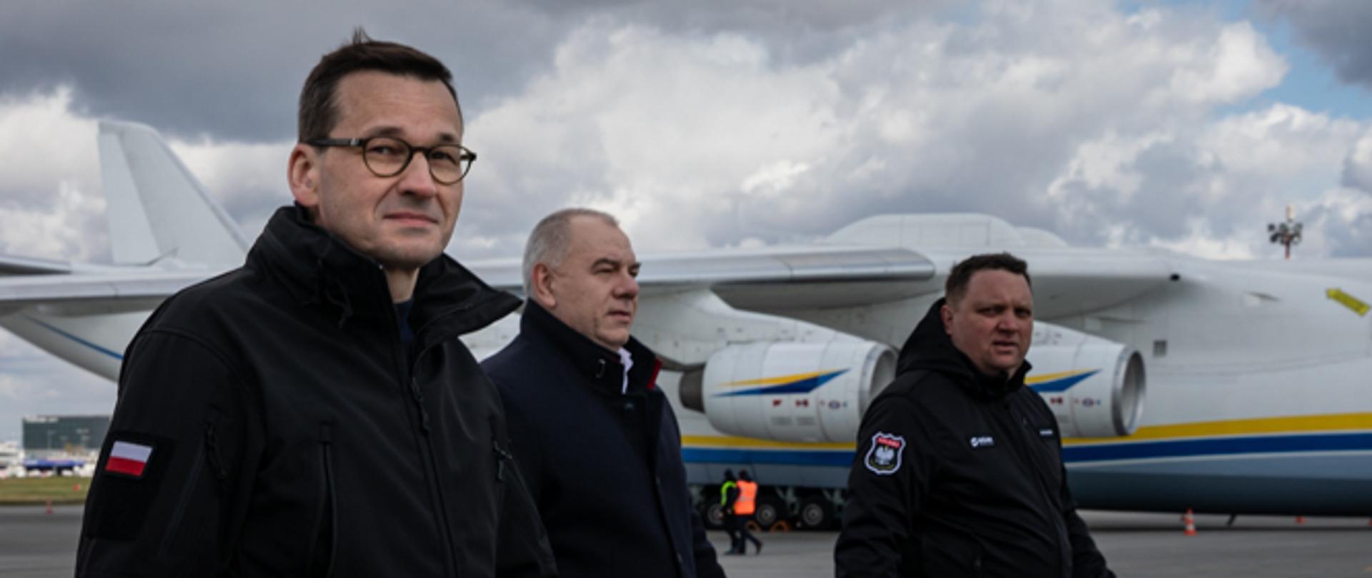 Premier Mateusz Morawiecki, Jacek Sasin i Marcin Chludziński idą na tle samolotu.