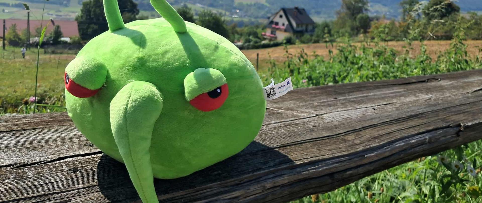 Zielona, pluszowa maskotka na tle górskiego krajobrazu