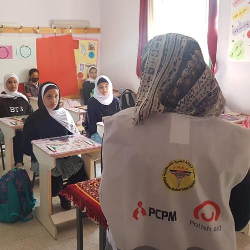 Szkolna klasa. Dziewczynki w hidżabach na głowach siedzą w ławkach. Przed nimi nauczycielka w chuście na głowie.