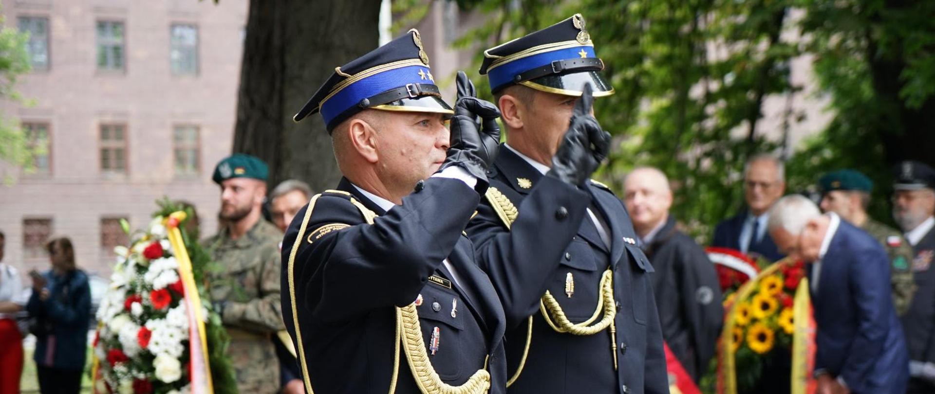Dwóch strażaków oddających honory stojąc.