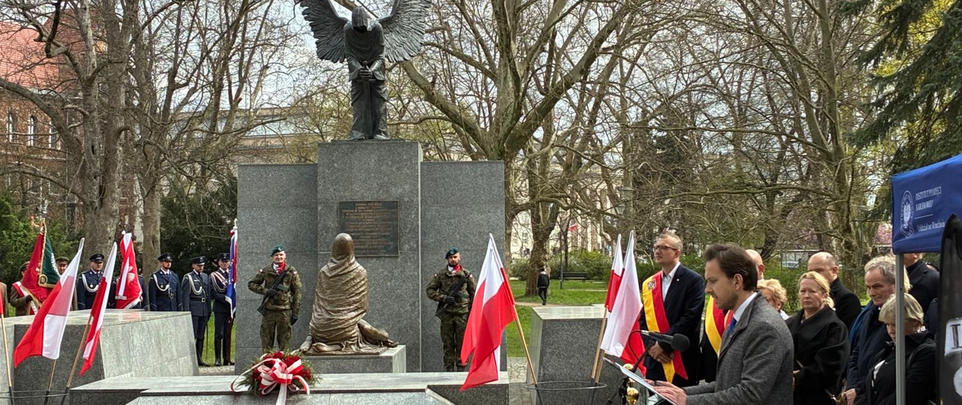Uczestnicy Obchodów Ofiar Zbrodni Katyńskiej stojący przy Pomniku wraz z osobą przemawiającą. 