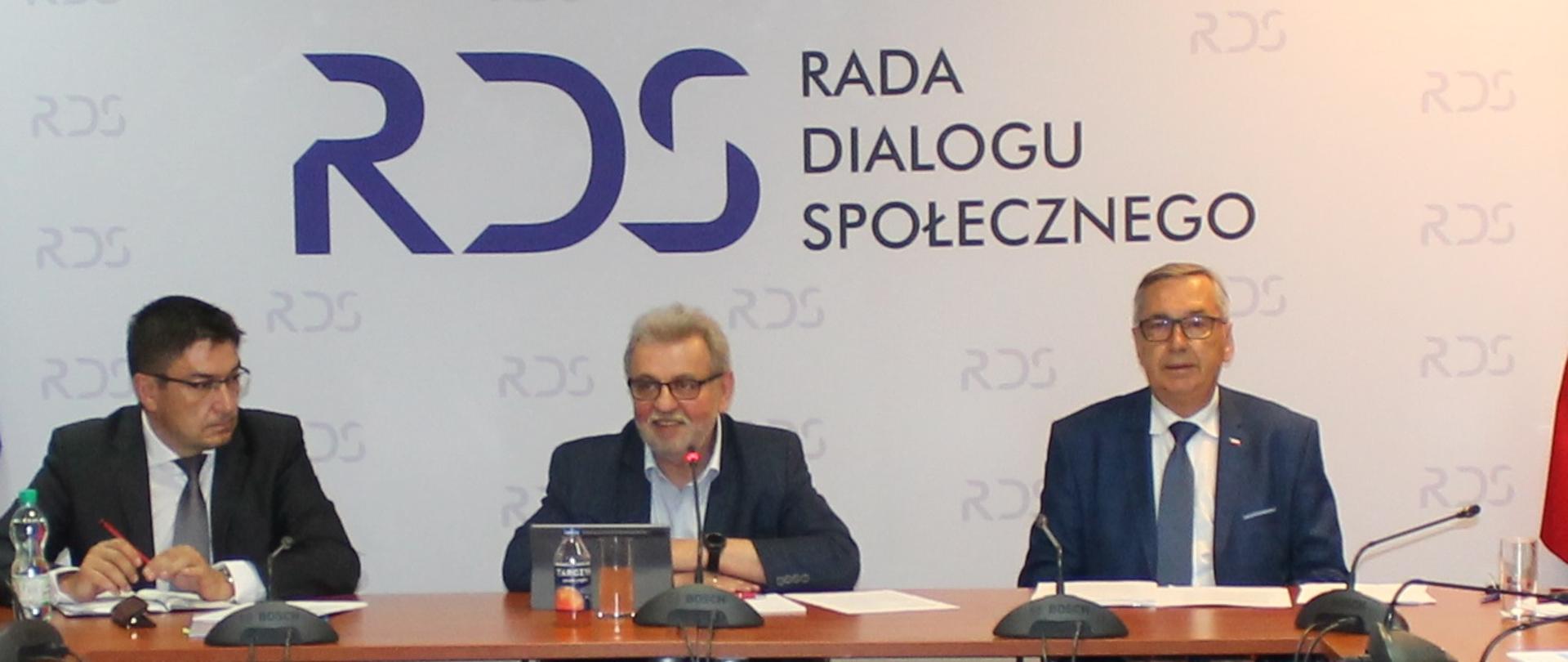 Zdjęcie przedstawia zasiadających za stołem prezydialnym: od lewej strony Przewodniczący Zespołu ds. rozwoju dialogu społecznego - Wojciech Ilnicki, Przewodniczący Zespołu ds. prawa pracy - Henryk Nakonieczny oraz Sekretarz Stanu w Ministerstwie Rodziny i Polityki Społecznej - Stanisław Szwed. Przed każdym z uczestników stoi mikrofon. W tle widnieje baner z napisem Rada Dialogu Społecznego. 