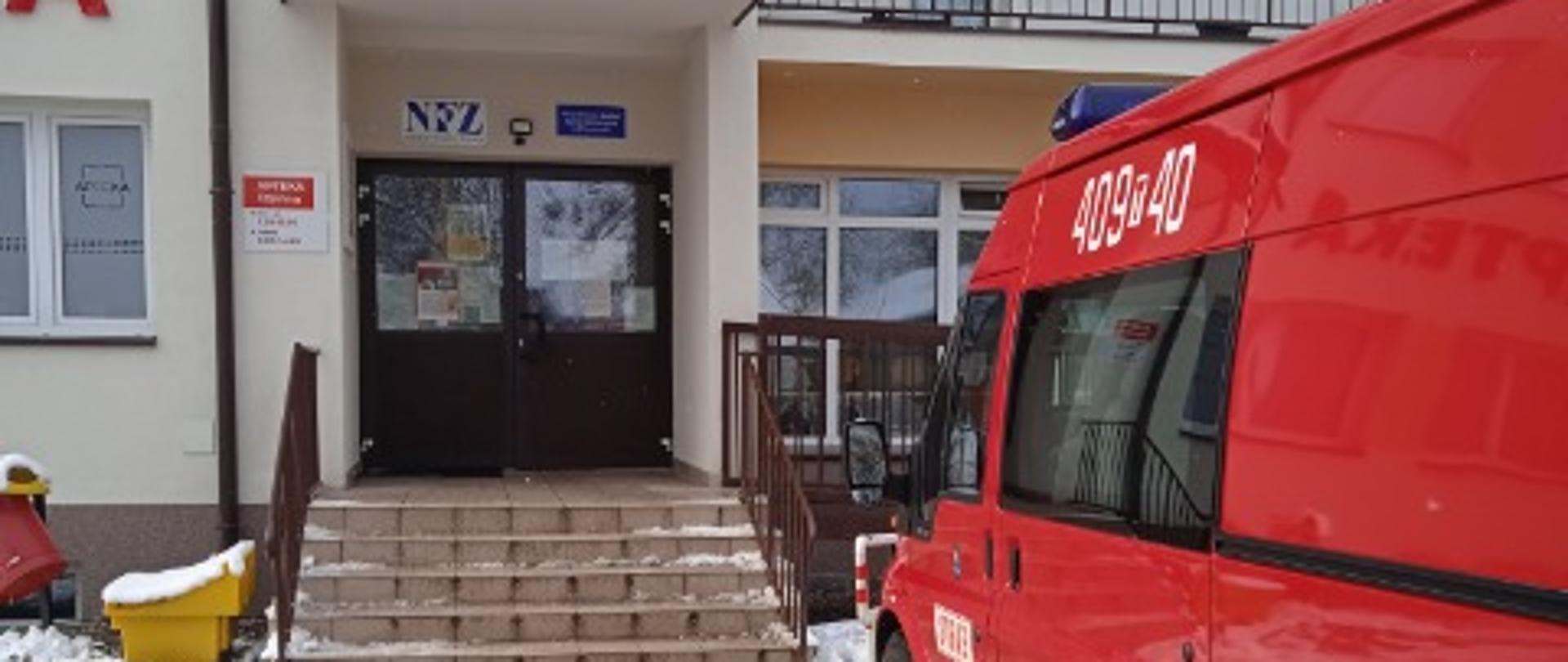 Zdjęcie przedstawia samochód pożarniczy, który dowiózł osoby na szczepienia do budynku ośrodka zdrowia.