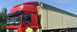 Inspektor ochrony środowiska i funkcjonariuszka służby celno-skarbowej prowadzą kontrolę ciężarówki. Rozmawiają z kierowcą przez okno kabiny.