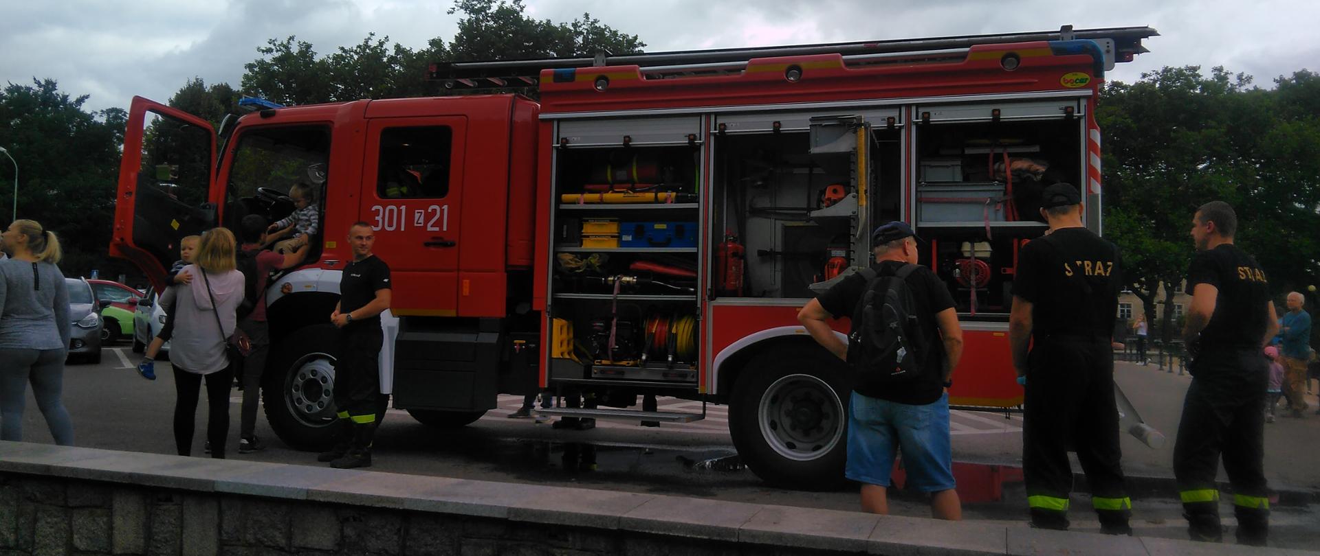 Widok bocznej części wozu bojowego z otwartymi drzwiami i skrytkami oraz ludzie oglądający wyposażenie samochodu